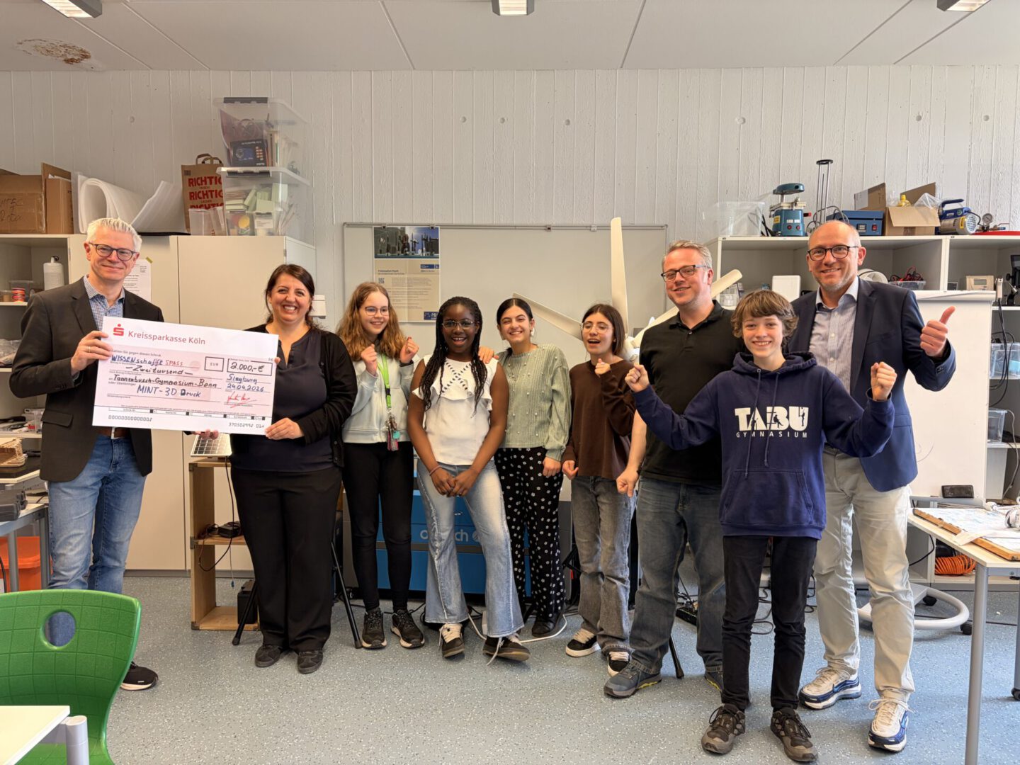 Christopher Risse überreicht Lehrerin Tuba Celik und den Schülerinnen und Schülern den symbolischen Scheck über die Spende von 2.000 Euro an das Tannenbusch-Gymnasium Bonn